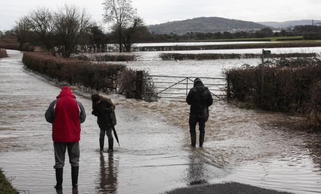 Three people wading on country road flooded by River Severn
